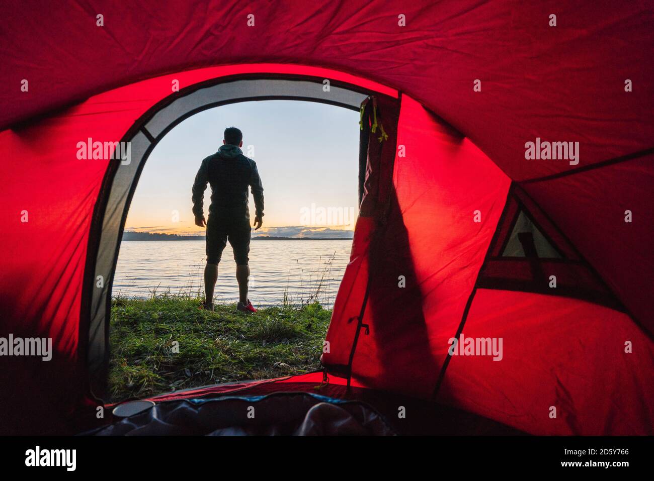 Mann, der in Estland zeltet, vor dem Zelt steht und den Sonnenuntergang beobachtet Stockfoto
