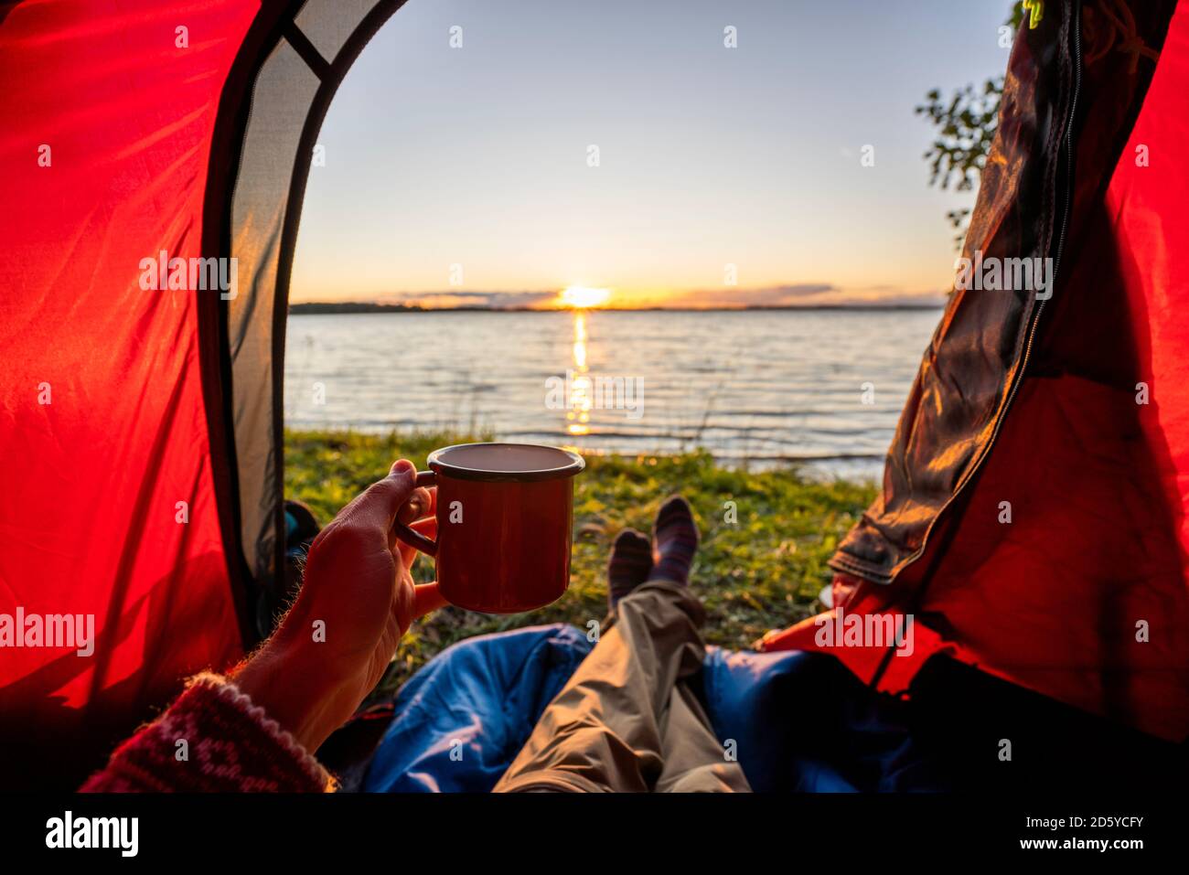 Mann, der in Estland zeltet und den Sonnenuntergang im Zelt beobachtet Stockfoto