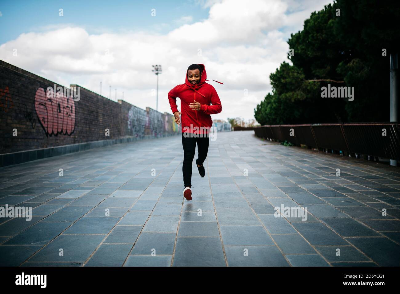 Lächelnder junge Mann tragen rote Hoodie läuft in der Stadt Stockfoto