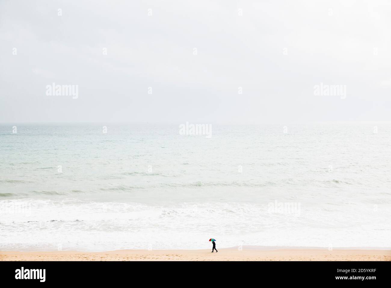 Spanien, Mallorca, eine Person mit Sonnenschirm am Strand entlang spazieren Stockfoto