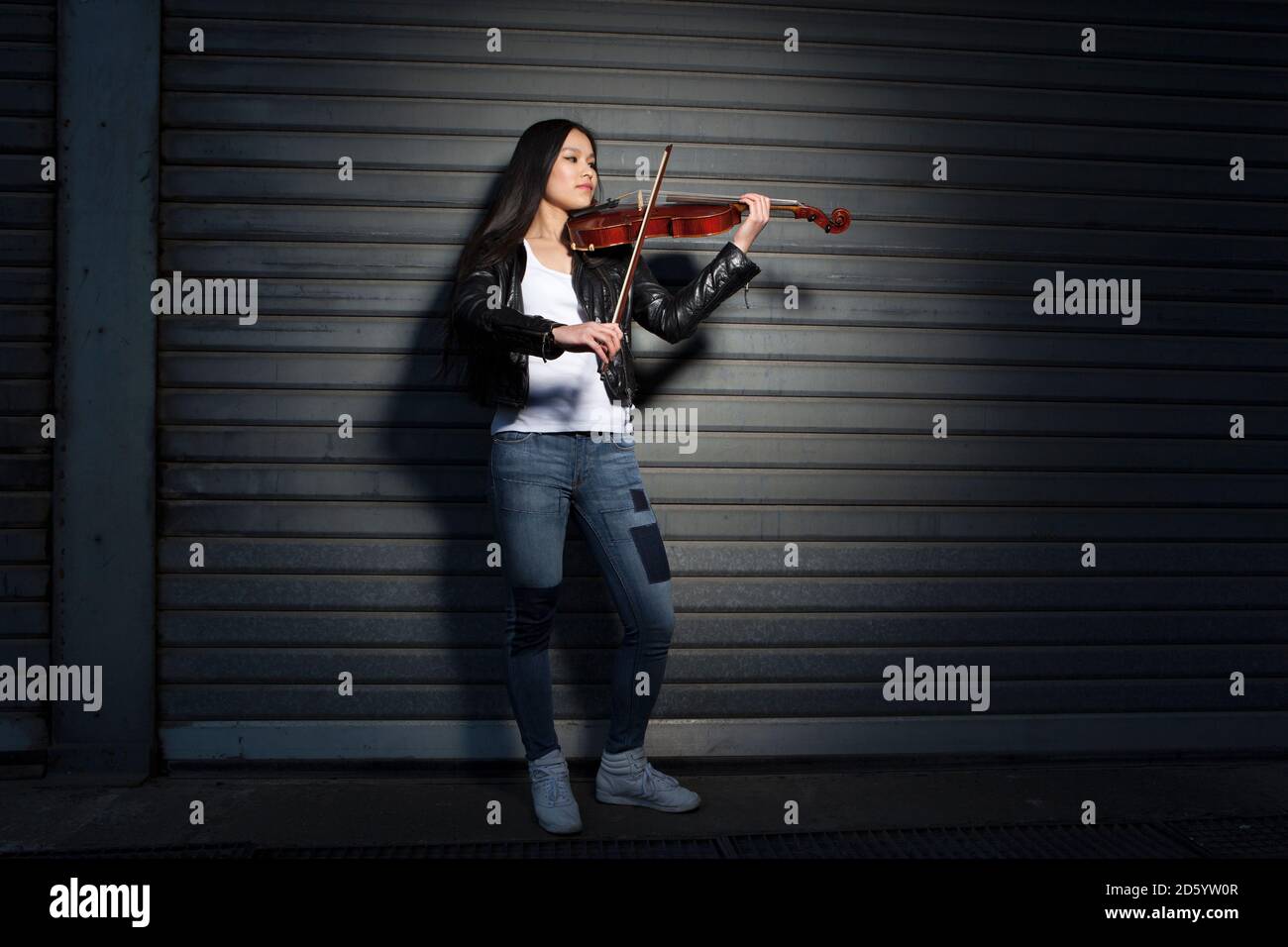 Junge weibliche asiatische spielen Geige vor einem Rollladen Stockfoto