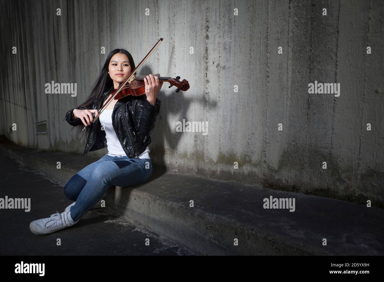 Junge weibliche asiatische spielen Geige vor Betonwand Stockfoto