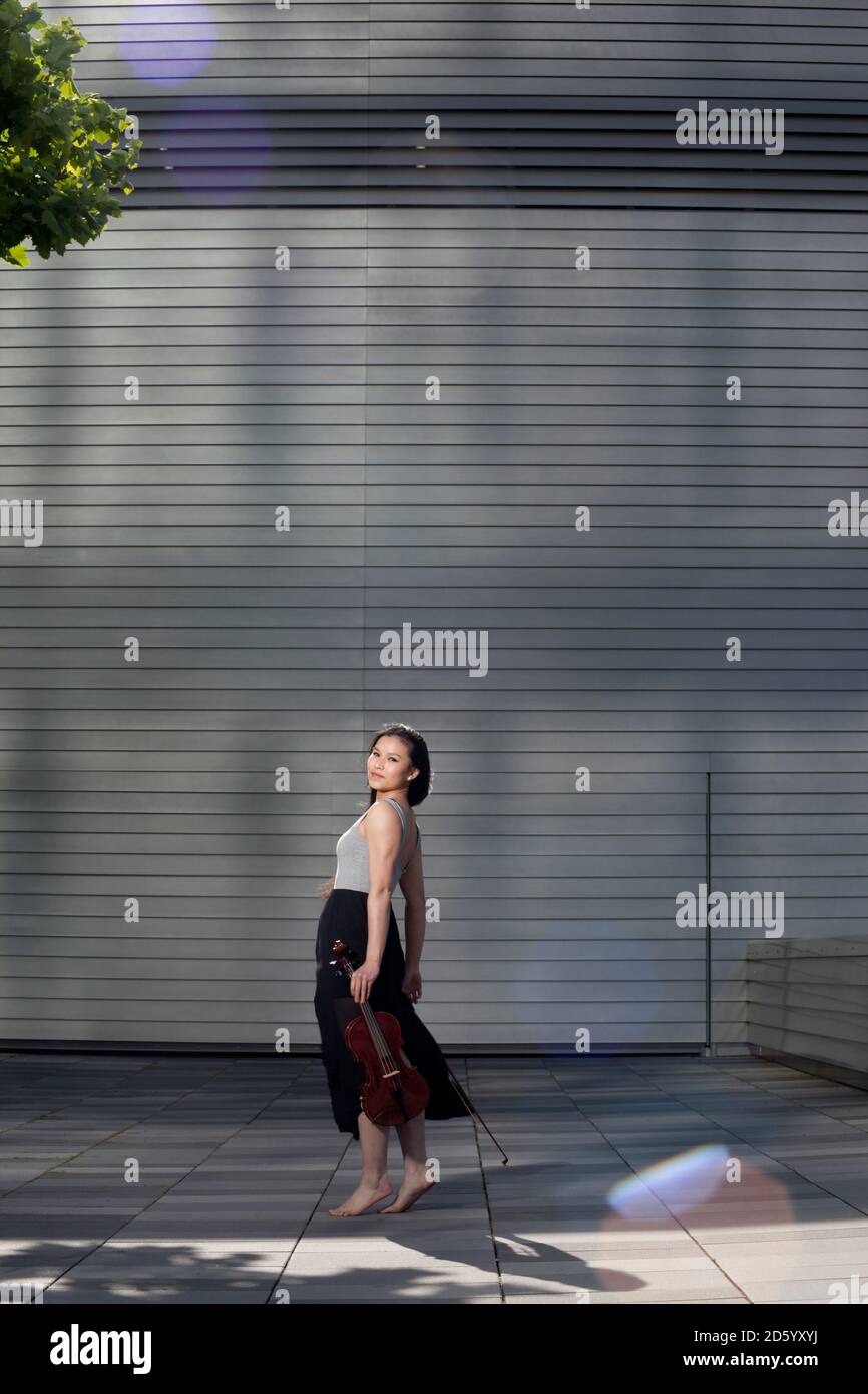 Junge weibliche asiatische mit Violine stand vor einer Fassade Stockfoto