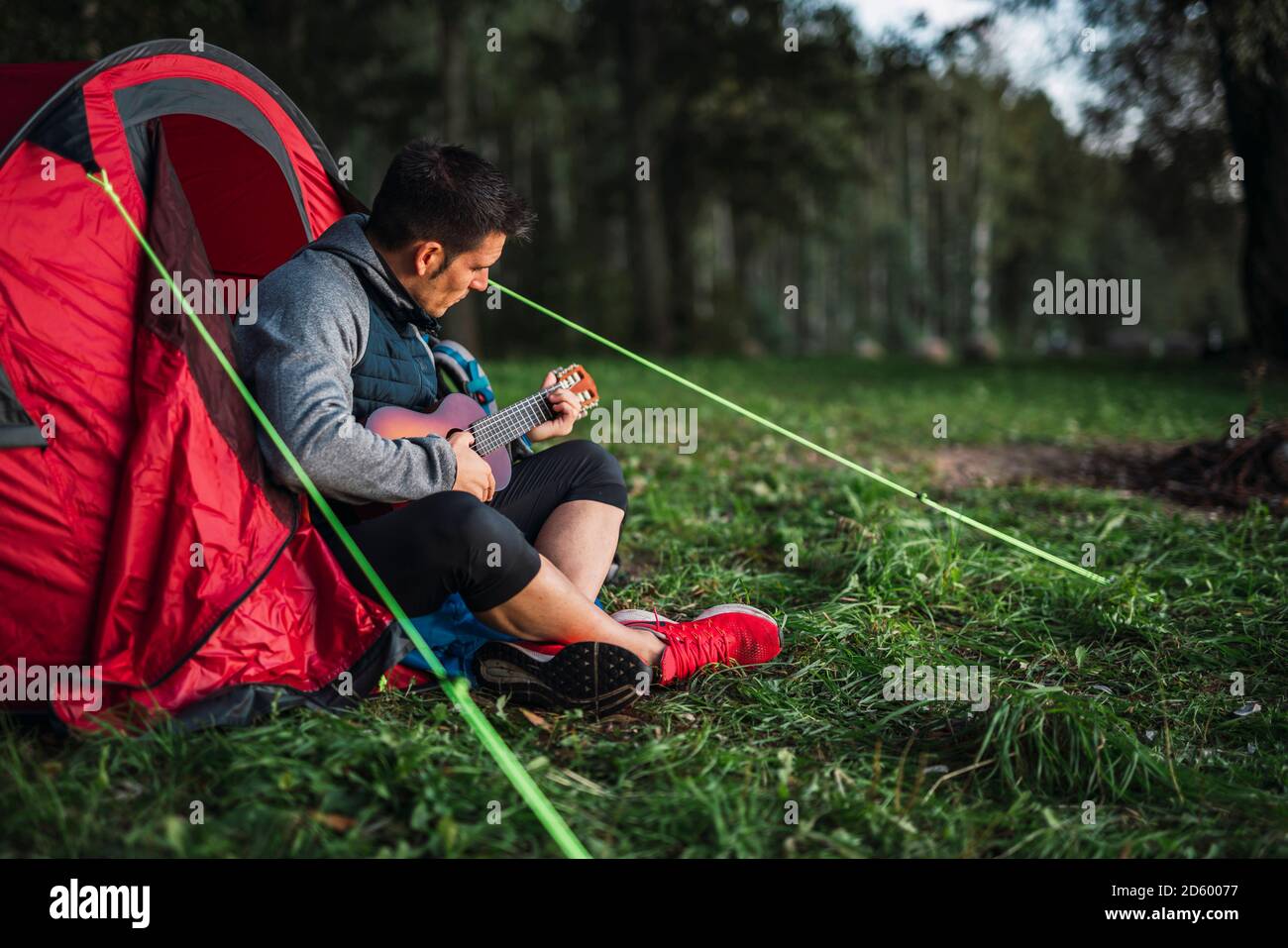 Mann, der in Estland zeltet, in seinem Zelt sitzt und die Ukulele spielt Stockfoto