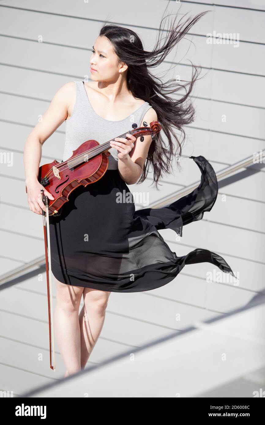 Junge weibliche asiatische mit Haar und Rock auf Treppen mit Geige stehend bläst Stockfoto