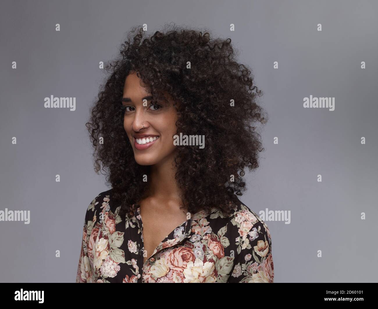 Porträt der lächelnde junge Frau mit Nasenring und Afro vor grauem Hintergrund Stockfoto