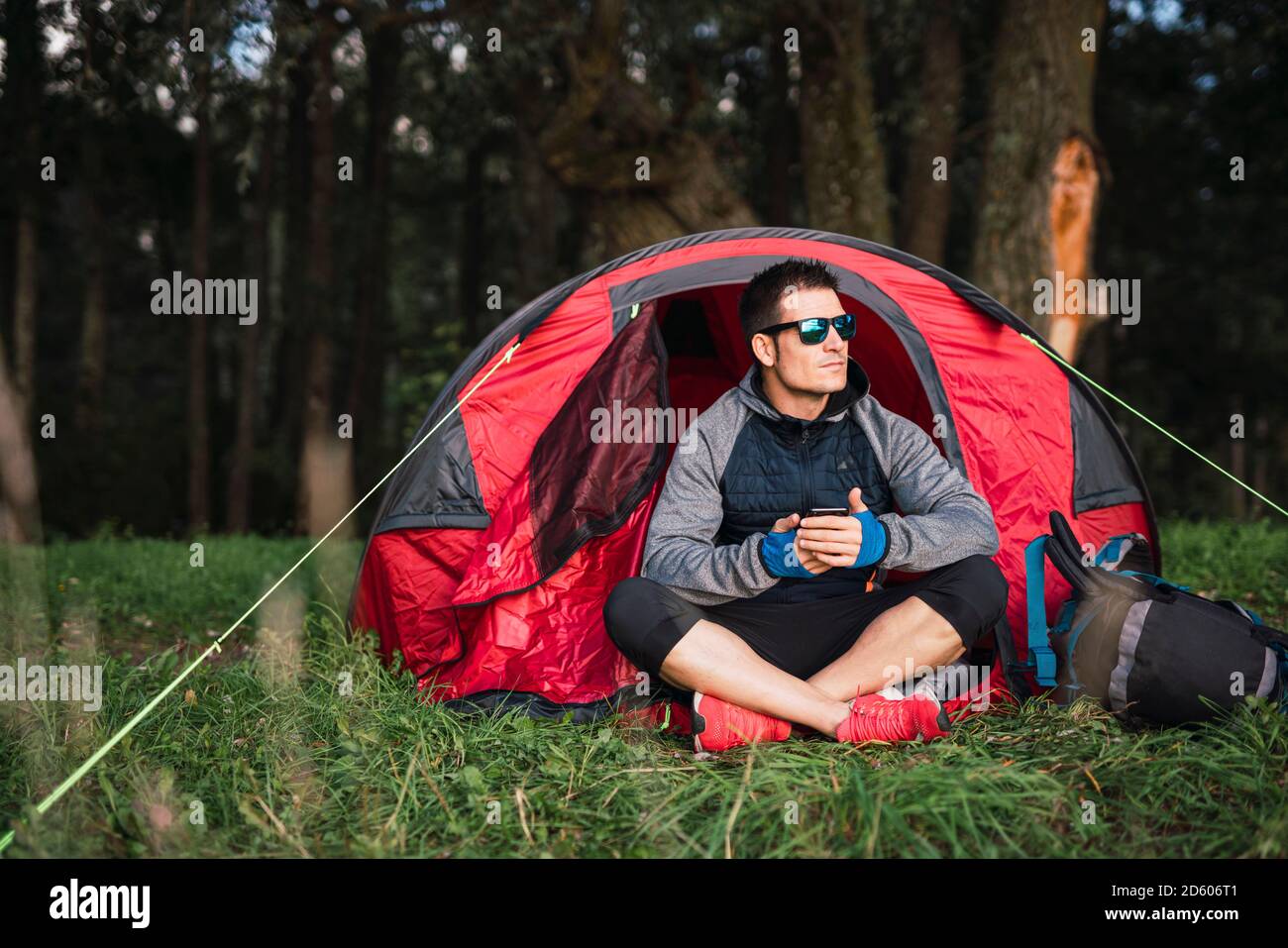 Mann, der in Estland zeltet, im Zelt sitzt, mit dem Smartphone Stockfoto