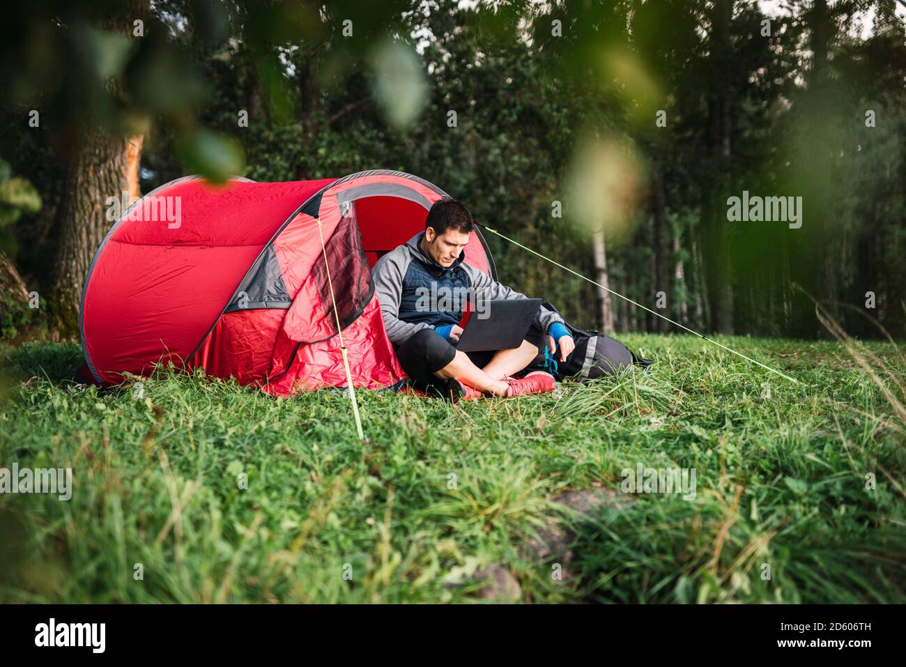 Mann, der in Estland zeltet, im Zelt sitzt, mit Laptop Stockfoto