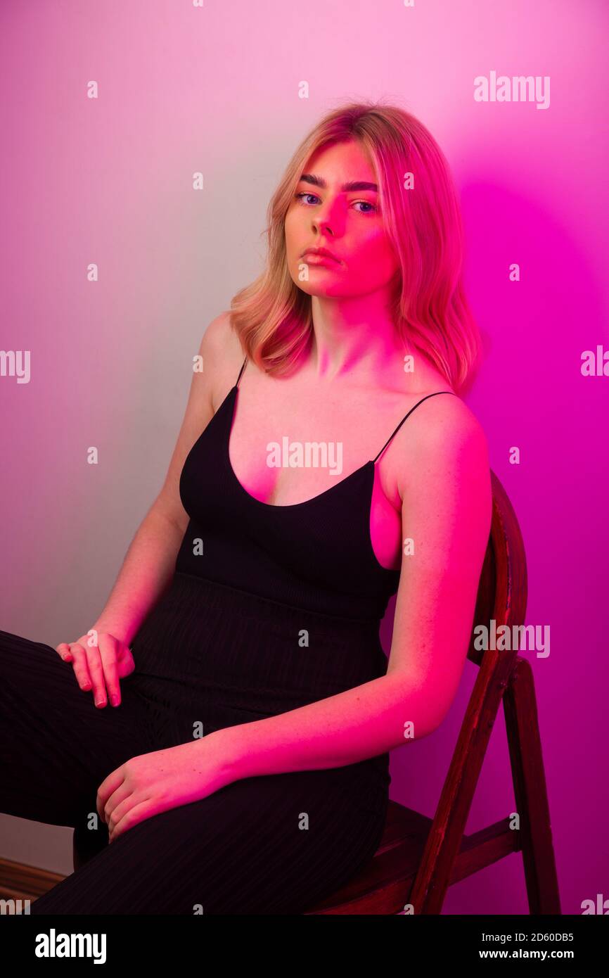Cool aussehende blonde Frau auf einem Stuhl von beleuchtet sitzen Rotes Licht Stockfoto
