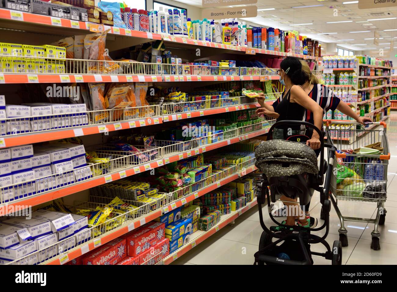 Frauen, die im Gang des Supermarkts einkaufen, schauen sich Reinigungsprodukte an, eines mit Kinderwagen, eines mit Einkaufswagen Stockfoto