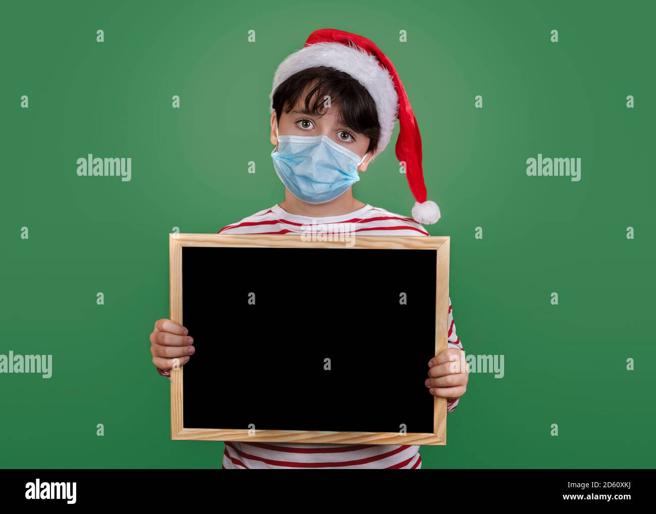 Frohe Weihnachten, lustiges Kind mit medizinischer Maske, die eine Tafel hält Grüner Hintergrund Stockfoto