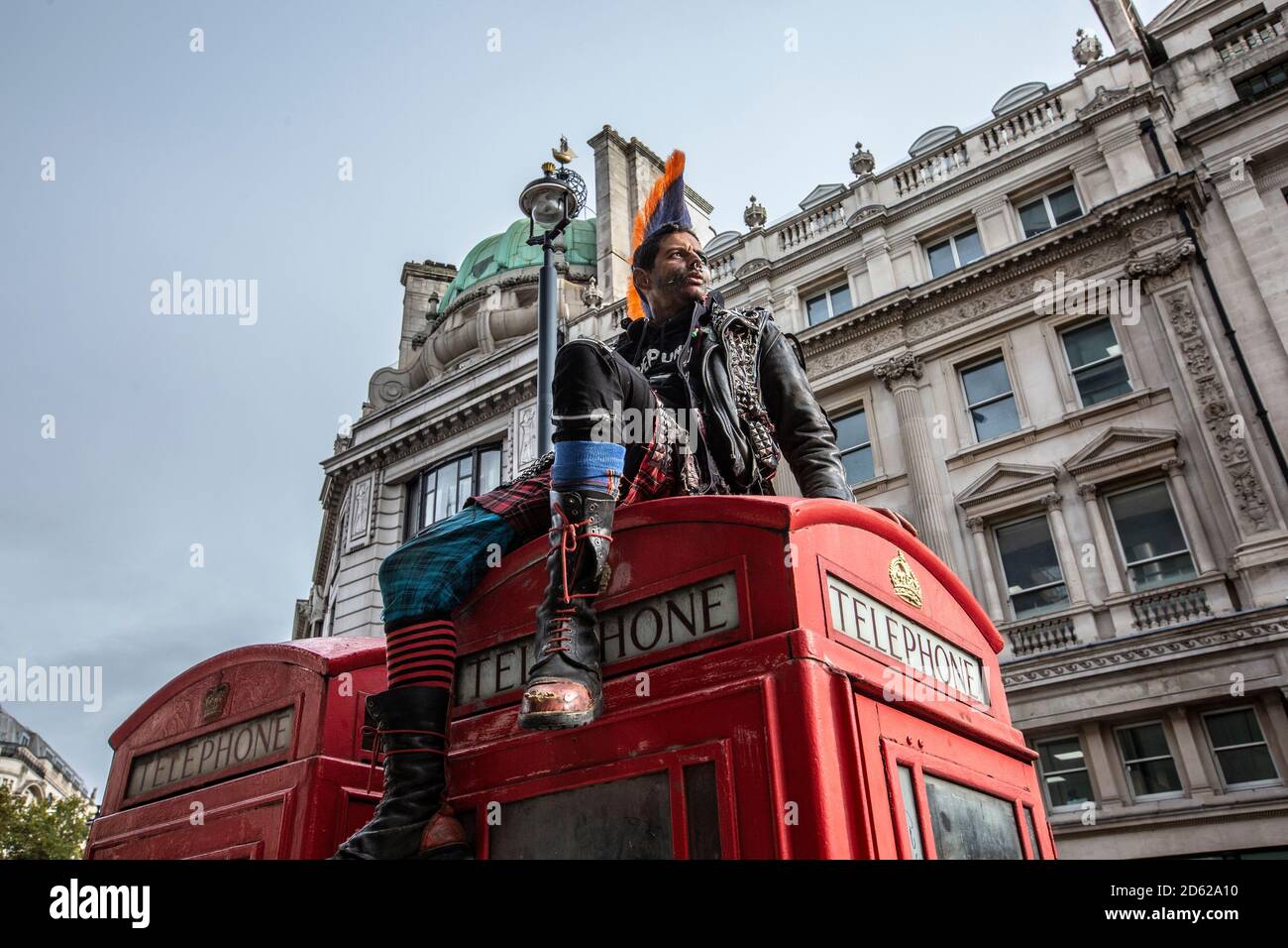 Punk-Rocker mit mohican-Haaren sitzt entspannt auf roten Telefonzellen im Zentrum von London, England, Großbritannien Stockfoto