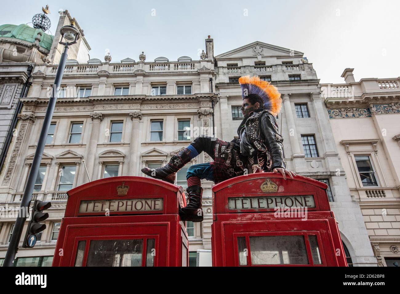 Punk-Rocker mit mohican-Haaren sitzt entspannt auf roten Telefonzellen im Zentrum von London, England, Großbritannien Stockfoto