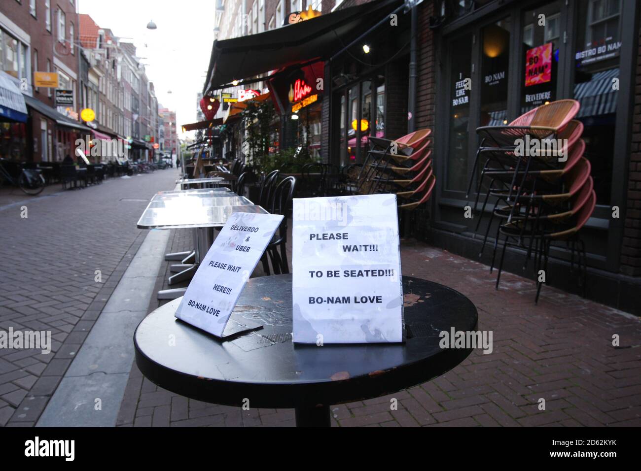 Ein Schild ‘bitte warten Sie, bis sie sitzen' auf den Tischen leer des geschlossenen Restaurants inmitten der Coronavirus-Pandemie am 14. Oktober 2020 in Amsterdam, Niederlande. Die niederländische Regierung kündigte an, dass ab heute neue strengere Maßnahmen zur Kontrolle neuer Infektionen zu versuchen. Der Alkoholverkauf wird nach 20 Uhr verboten, und die Bewohner dürfen maximal drei Gäste pro Tag zu Hause empfangen. Alle Cafés, Bars und Restaurants müssen um 22 Uhr schließen und Gesichtsmasken sind in allen öffentlichen Innenräumen obligatorisch. (Foto von Paulo Amorim/Sipa USA) Stockfoto