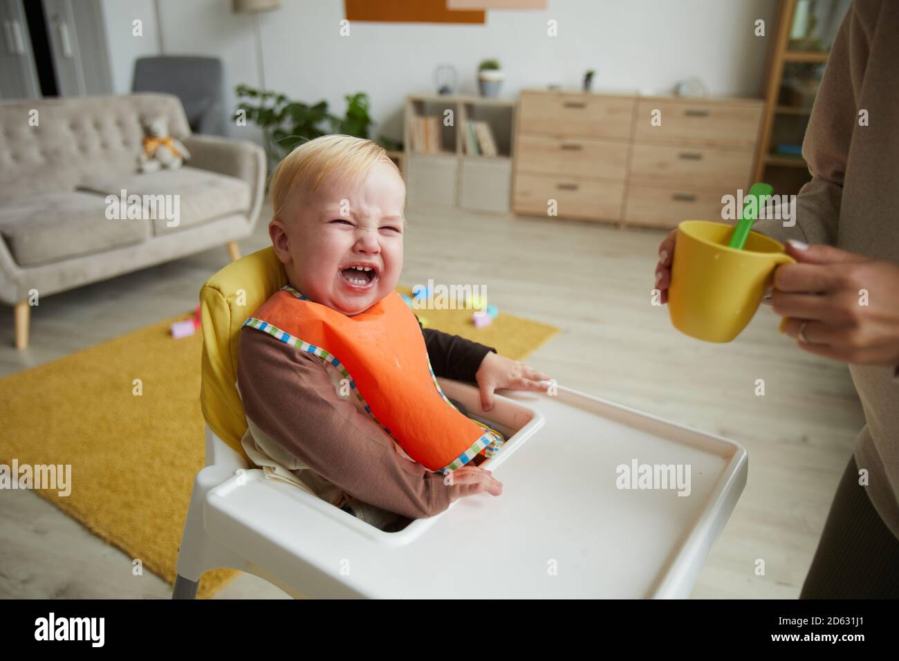 Cute Baby junge tragen Lätzchen sitzend Babystuhl, während seine Mutter  füttert ihn in der Küche Stockfotografie - Alamy
