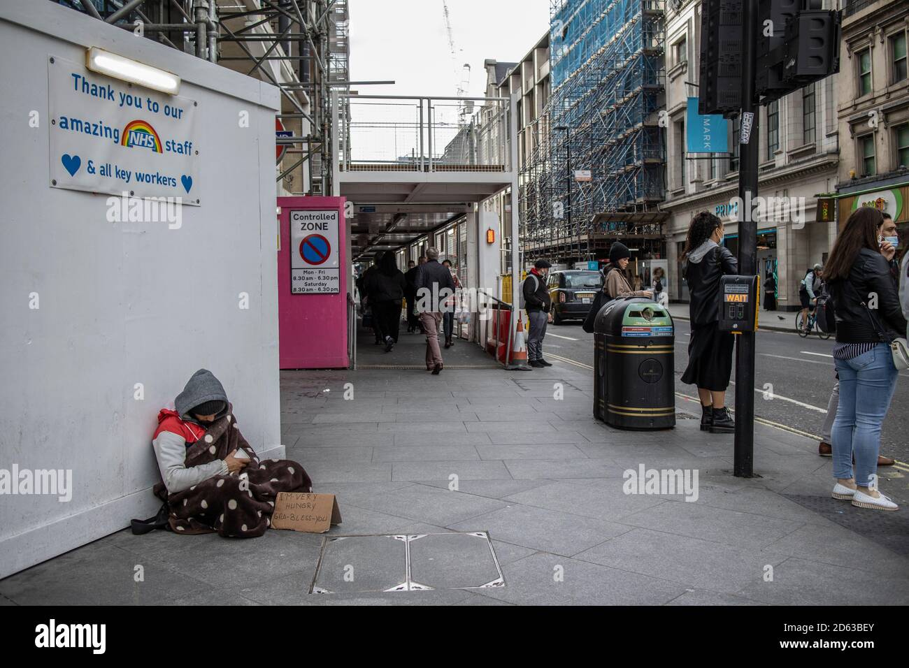 Obdachloser Mann sitzt bettelnd um Geld unter einem "Danke NHS" Schild, das an einem Arbeiter-Horten auf der Oxford Street, London, West End, England, Großbritannien angebracht ist Stockfoto