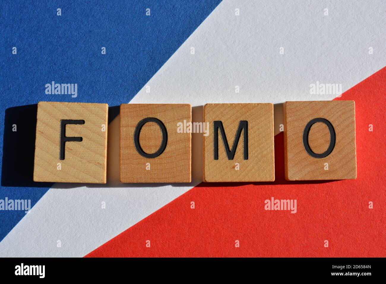 FOMO Akronym für Angst vor dem Verfehlen in Holzbuchstaben auf rotem, weißem und blauem Hintergrund Stockfoto