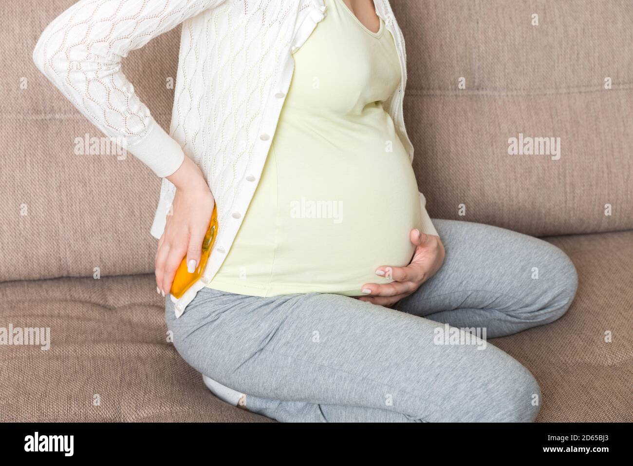 Schwangere Frau leiden unter Rückenschmerzen hält eine heiße Flasche oder einen warmen wärmer gegen ihren Rücken. Konzept schwangere Frau Lebensstil und Gesundheitsversorgung. Stockfoto
