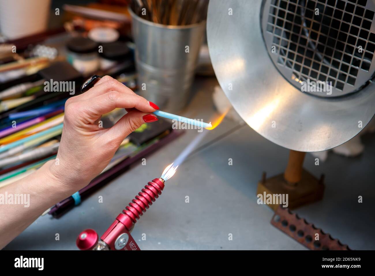 Der Künstler erhitzt das Glas mit einem Gasbrenner. Der Prozess der Herstellung von Glasschmuck. Die Hände des Meisters aus der Nähe Stockfoto