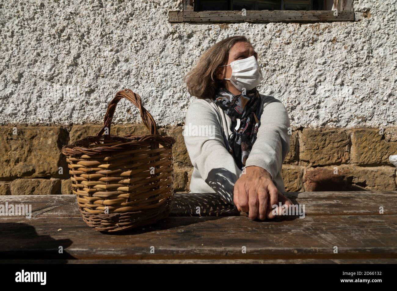 Eine ältere Frau, die eine weiße Schutzmaske trägt, streckt ihre Arme und entspannt sich in der Nähe der Berghütte des Brunnens von Artica, in Luesia, Spai Stockfoto