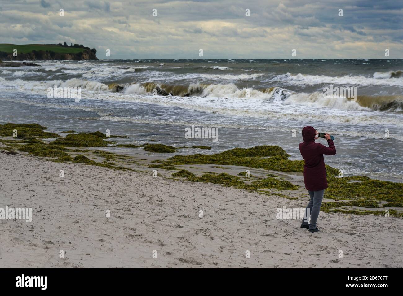 Frau macht Fotos von wilden Wellen im Sturm und Onshore-Wind am Strand von Boltenhagen an der Ostsee in Deutschland, Kopierraum, ausgewählter Fokus, Narro Stockfoto