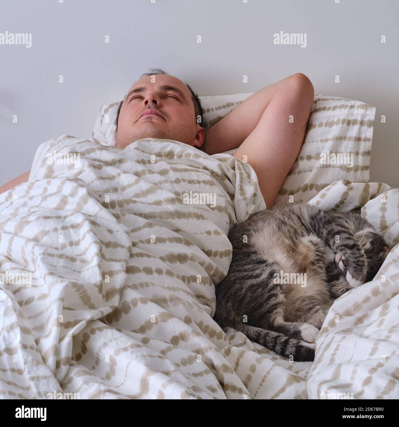 Ein Mann schläft auf einem Bett mit einer Katze, echten Lebensstil. Nicht inszeniertes Foto Stockfoto