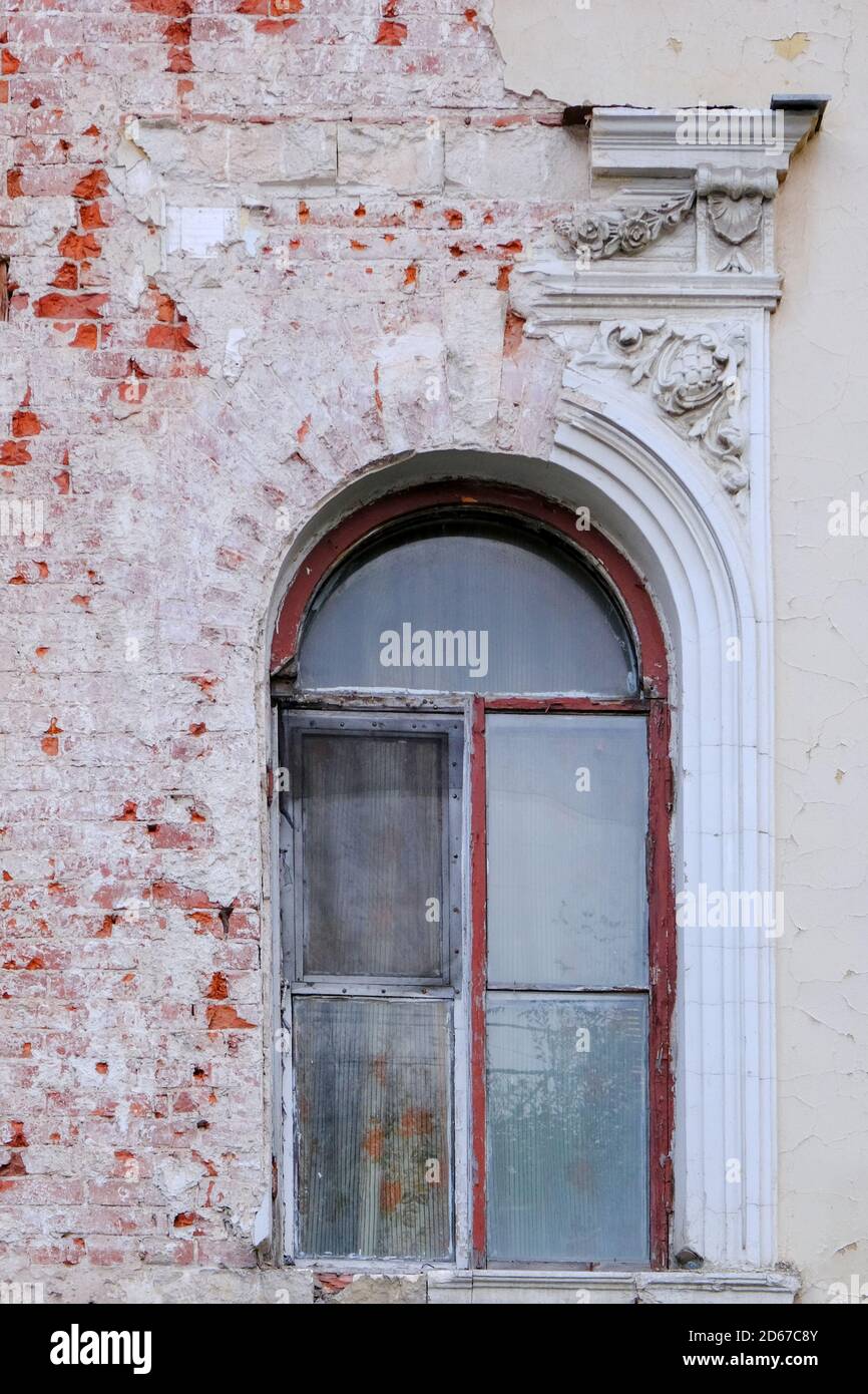 Fragment der Fassade und gewölbtes Fenster mit ruinierten Stuckarbeiten eines alten verlassenen Gebäudes. Stockfoto