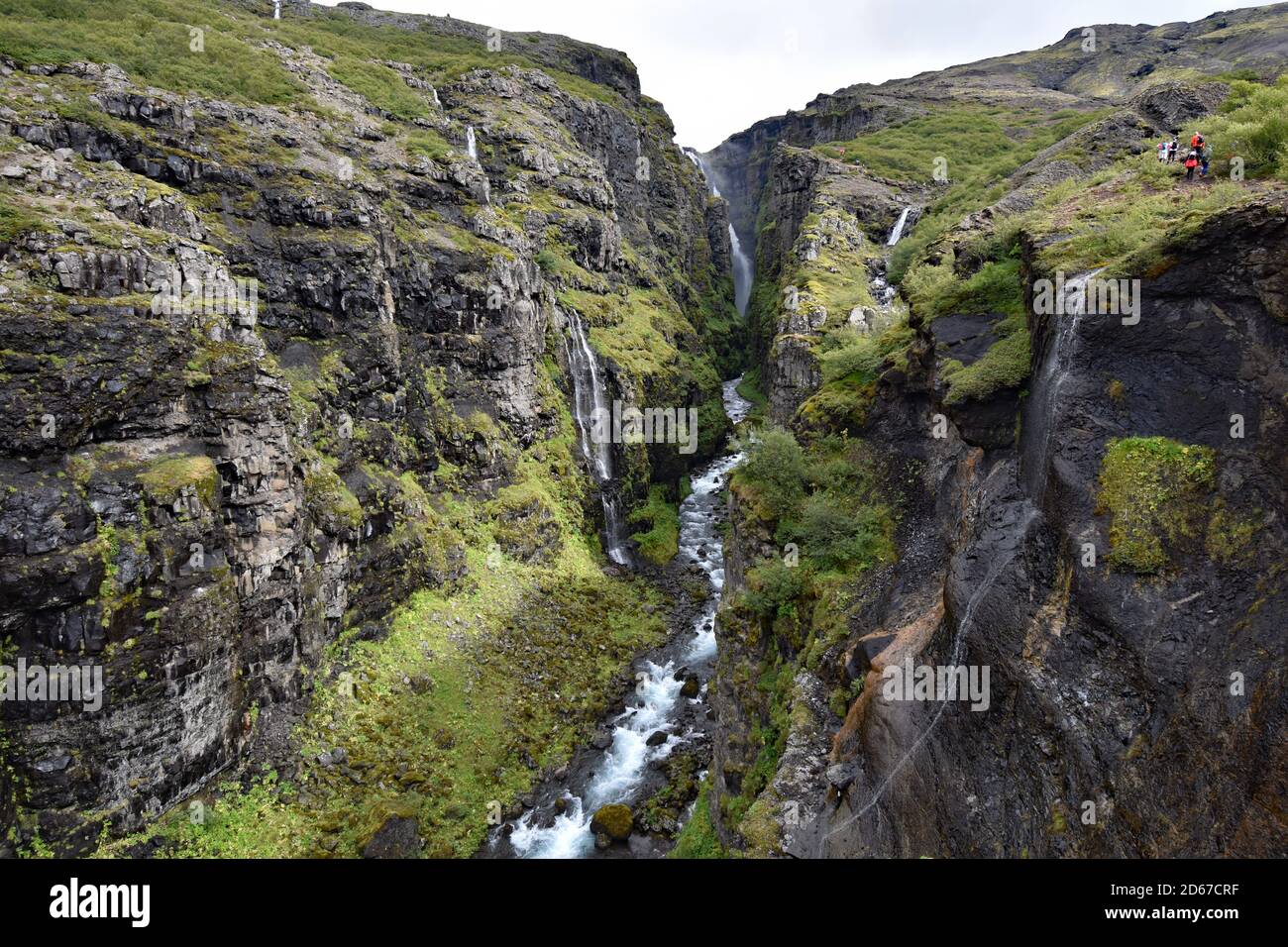 Ein Fluss fließt in der Schlucht weg von Glymur Wasserfall in Hvalfjordur, West Island. Wanderer können auf dem Weg entlang des Randes der Schlucht gesehen werden Stockfoto