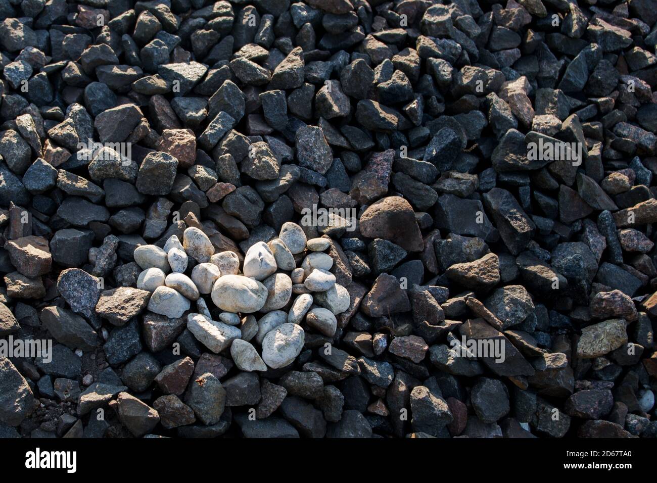 Das Herz ist aus weißen Steinen auf dunkelbraunem und grauem Granit des Bahndamms gelegt. Konzept: Sanft, Gefühl vor dem Hintergrund der rauen Realität Stockfoto