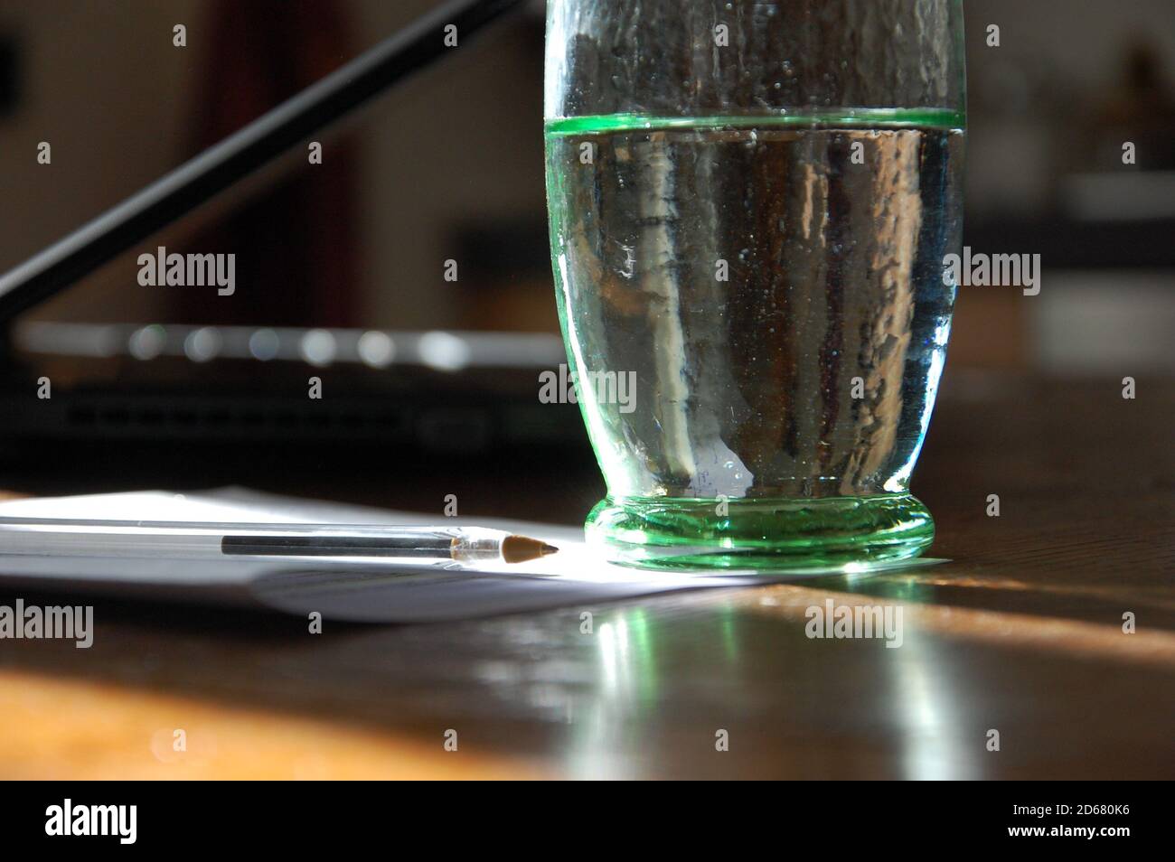 Ein grünes Glas voll Wasser auf dem Küchentisch und einige Papiere und ein Stift zur Seite und ein Computer in verschwommenem Hintergrund. Das Leben zu Hause in covid19 mal. Stockfoto