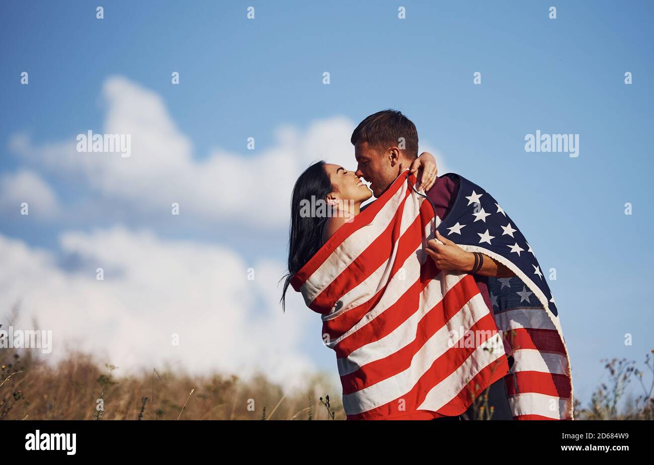 Küssen sich gegenseitig. Fühlt Freiheit. Schönes Paar mit amerikanischer Flagge haben eine gute Zeit im Freien auf dem Feld Stockfoto