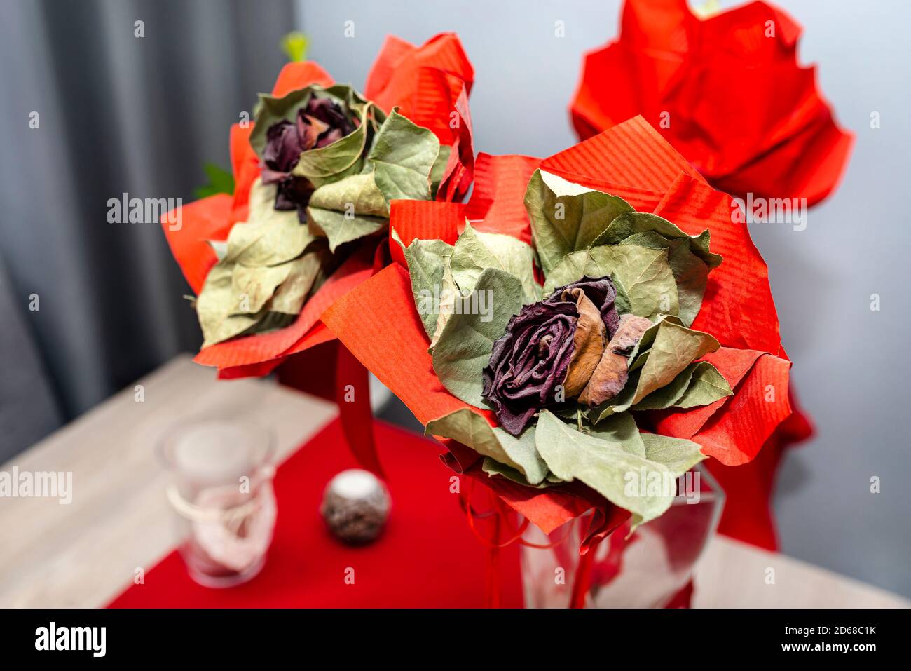 Eine verwelkte rote Rose mit einem großen roten Band, das auf einem Tisch in einer Vase steht. Stockfoto