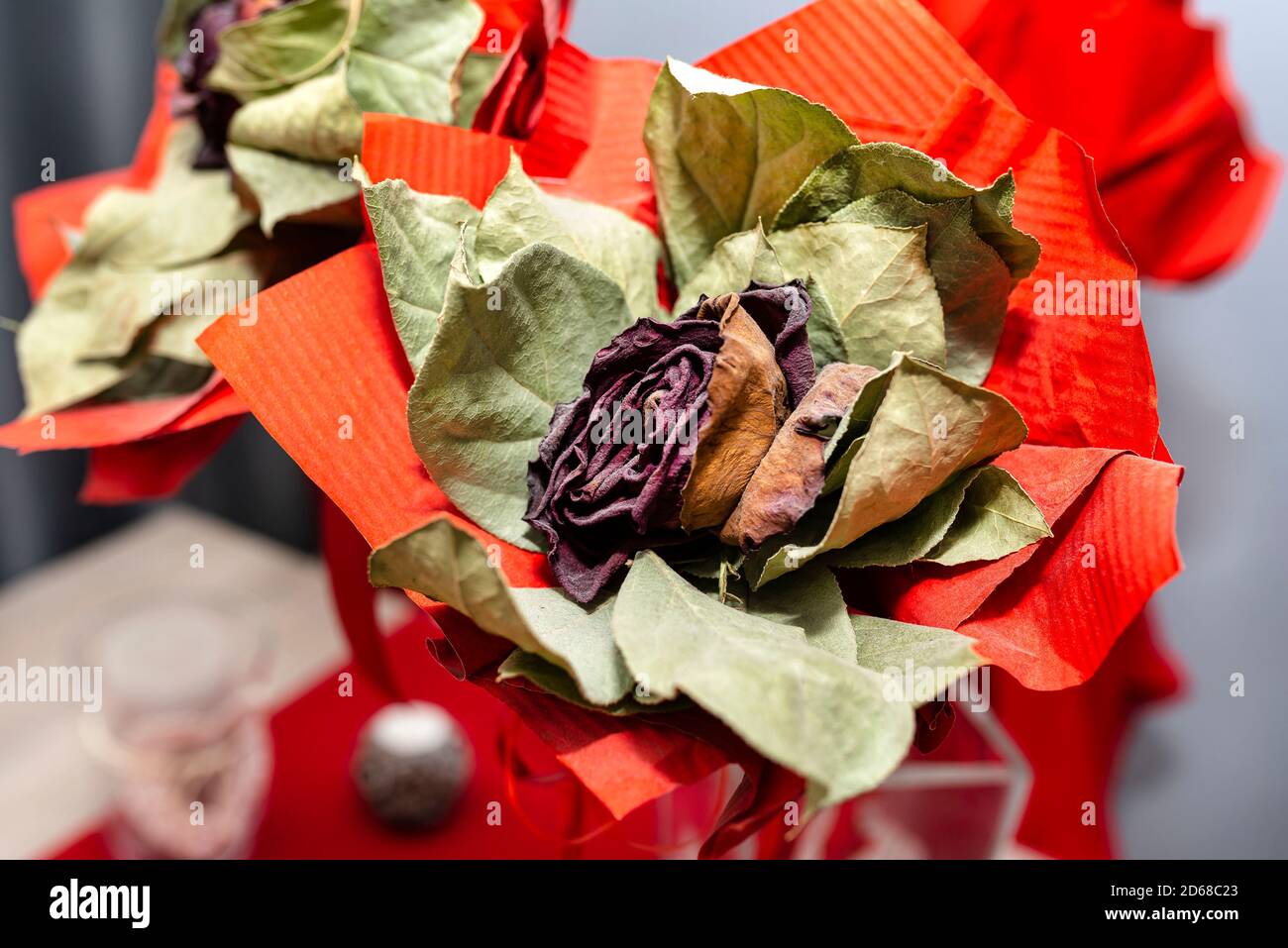 Eine verwelkte rote Rose mit einem großen roten Band, das auf einem Tisch in einer Vase steht. Stockfoto