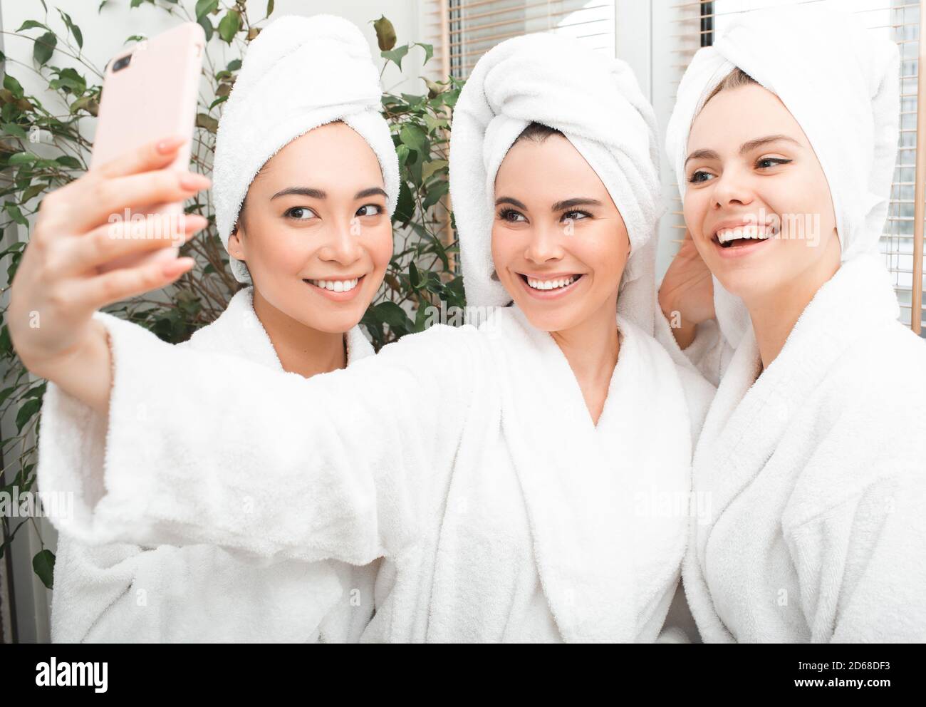 Frauen haben ein schönes Wochenende im Spa Resort. Drei schöne Frauen tragen Bademäntel und Handtücher auf dem Kopf machen Selfie, genießen Ruhe Stockfoto