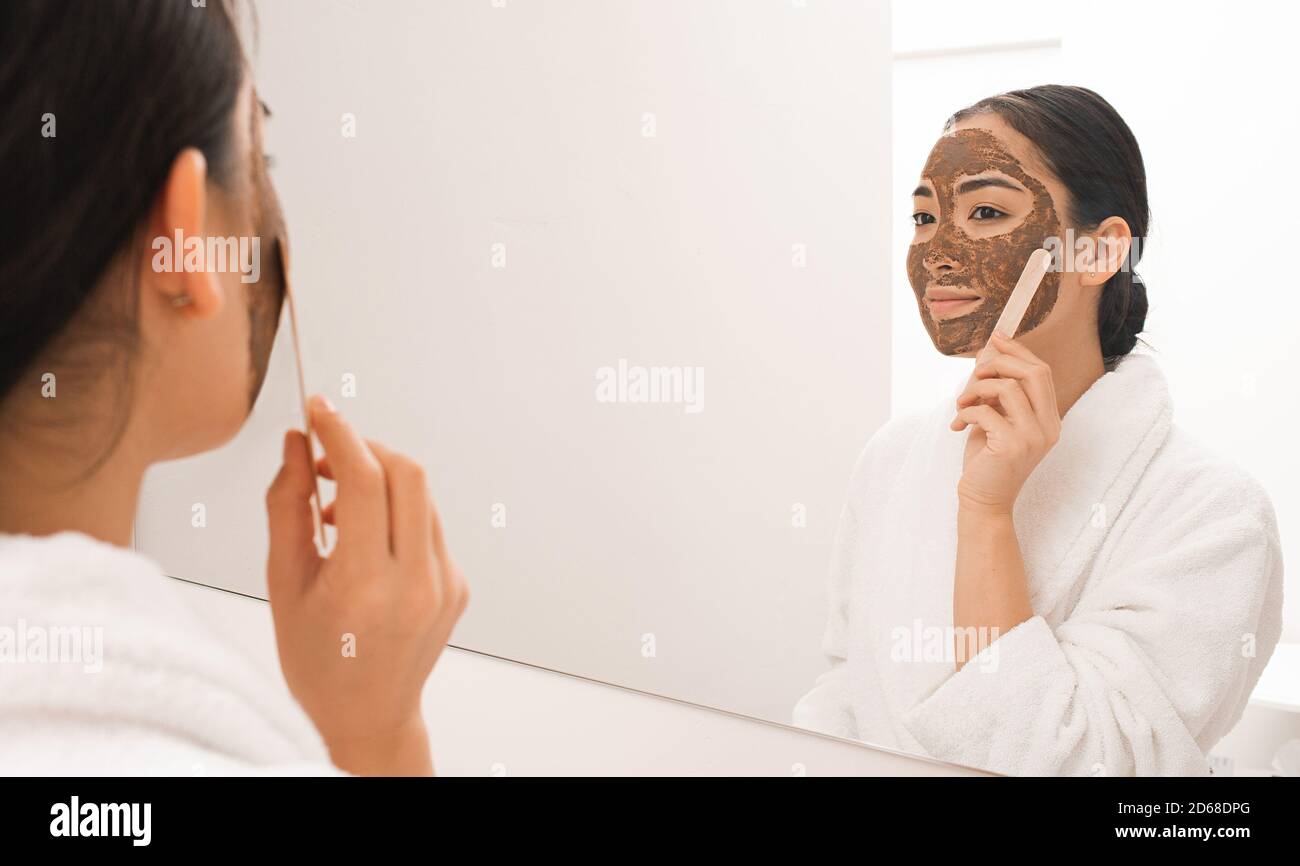 Frau, die eine Schlammmaske auf ihr Gesicht aufwendet. Behandlung, Reinigung und Erweichung der Haut. Teil einer Serie mit Schlammmaske Stockfoto