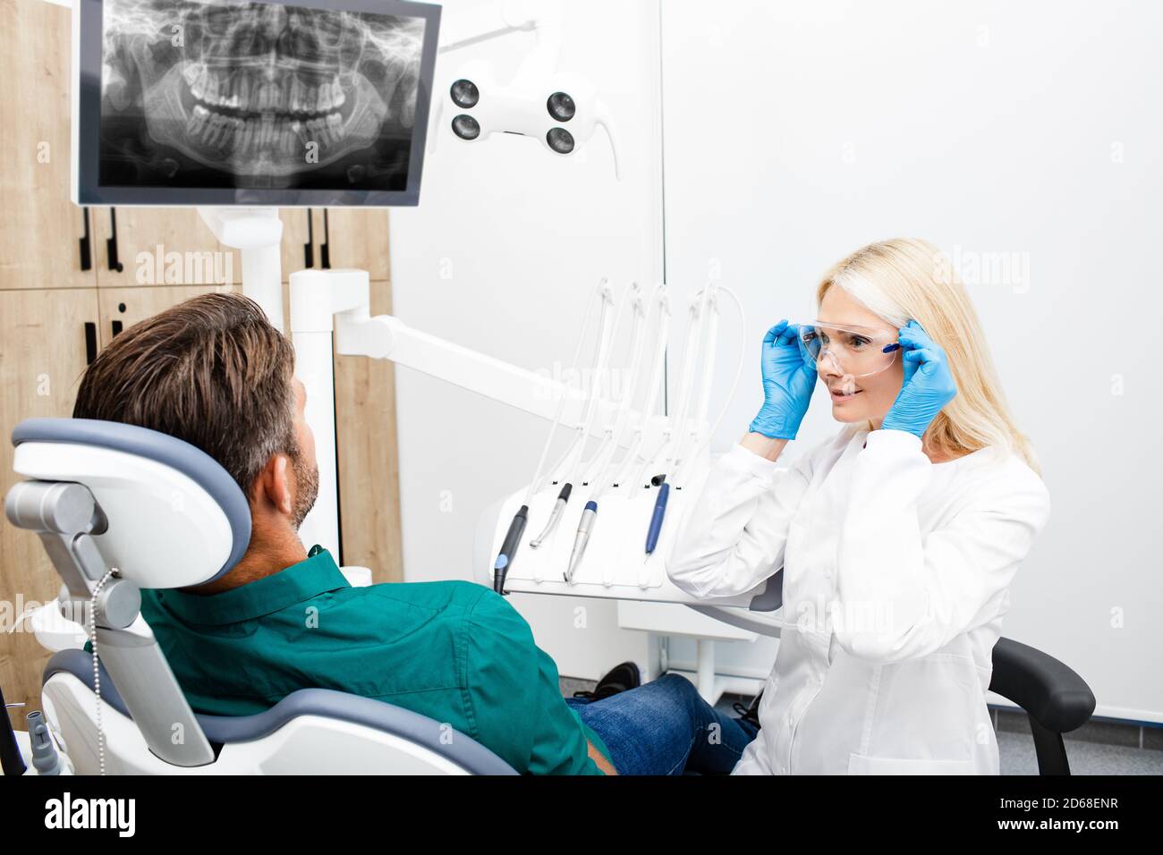 Frau Zahnarzt bereitet sich auf die Arbeit mit dem männlichen Patienten. Zahnärztin, die Schutzbrille während ihres Arbeitsplatzes justiert Stockfoto
