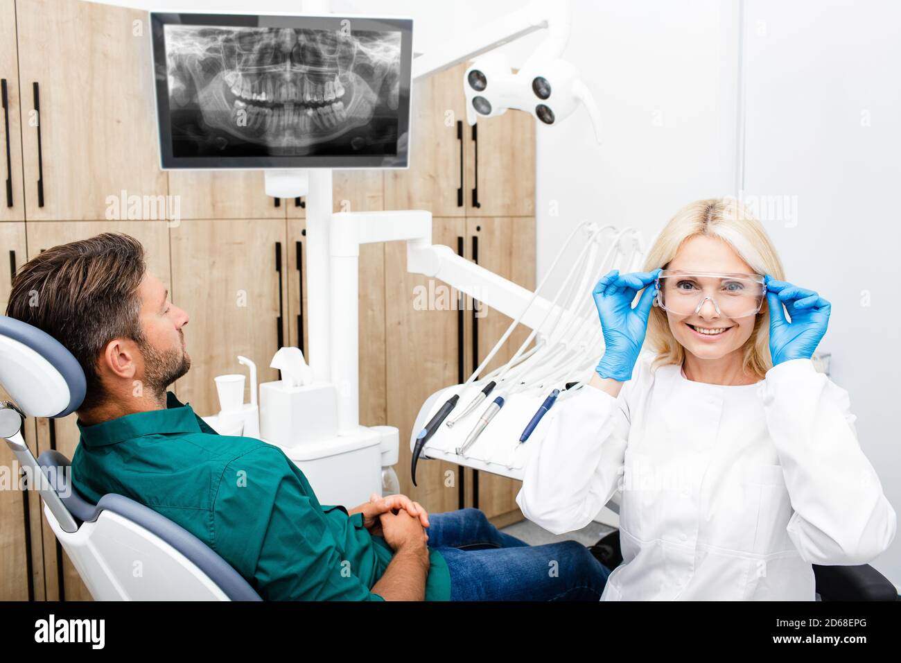 Frau Zahnarzt bereitet sich auf die Arbeit mit dem männlichen Patienten. Zahnärztin, die Schutzbrille während ihres Arbeitsplatzes justiert Stockfoto