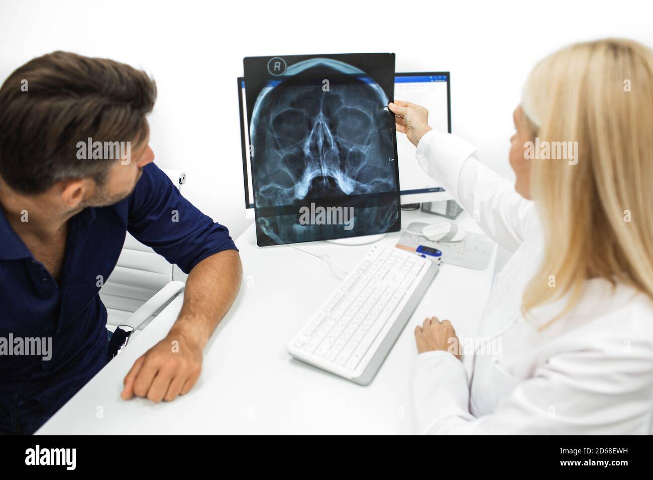 Arzt, der einem Patienten während einer Konsultation eine Röntgenaufnahme ihres Kopfes und der Kieferhöhlen zeigt. Diagnostik und Behandlung von Sinusitis und frontalen s Stockfoto