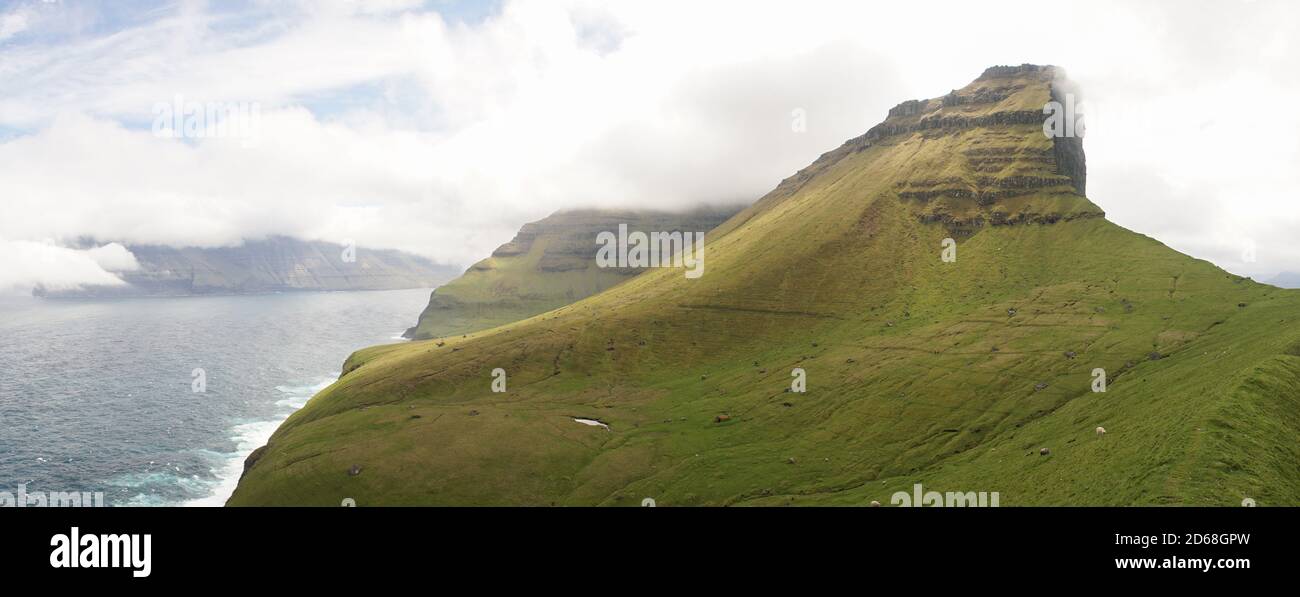 Kallur Leuchtturm auf der Insel Kalsoy mit grünen, üppigen Klippenlandschaften und Wanderern für die Perspektive auf den Färöer Inseln, Dänemark. Stockfoto