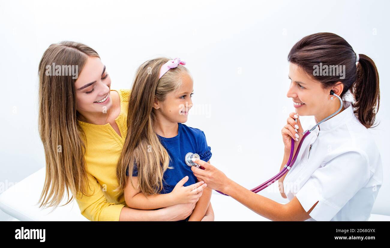 Der Kinderarzt überprüft die Lunge und das Herz des Kindes mit einem Stethoskop. Kleines Mädchen auf den Armen der Mutter während der medizinischen Untersuchung im Krankenhaus sitzen Stockfoto