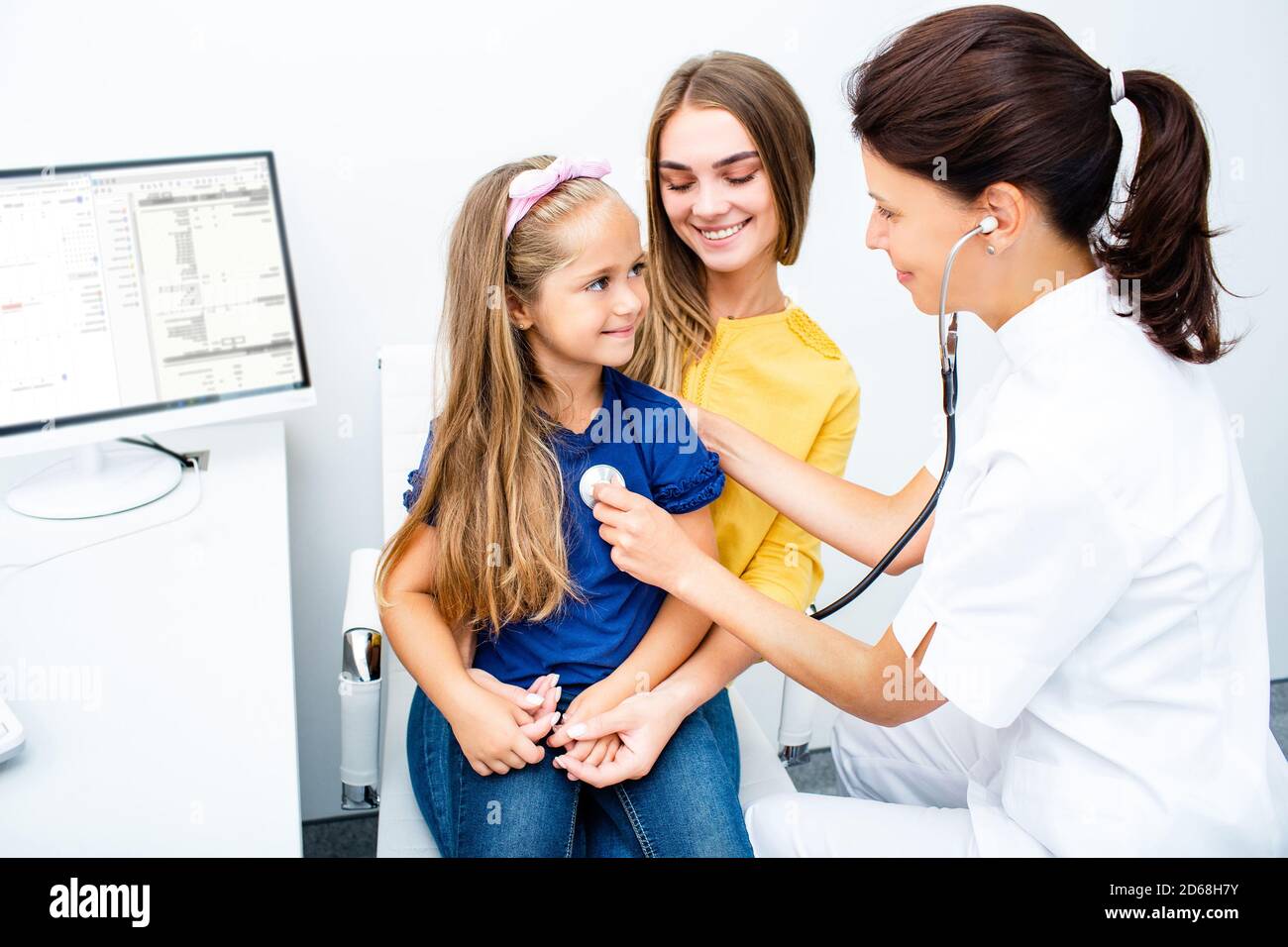 Der Kinderarzt überprüft die Lunge und das Herz des Kindes mit einem Phonendoskop. Kleines Mädchen auf den Armen der Mutter während der medizinischen Untersuchung im Krankenhaus sitzen Stockfoto