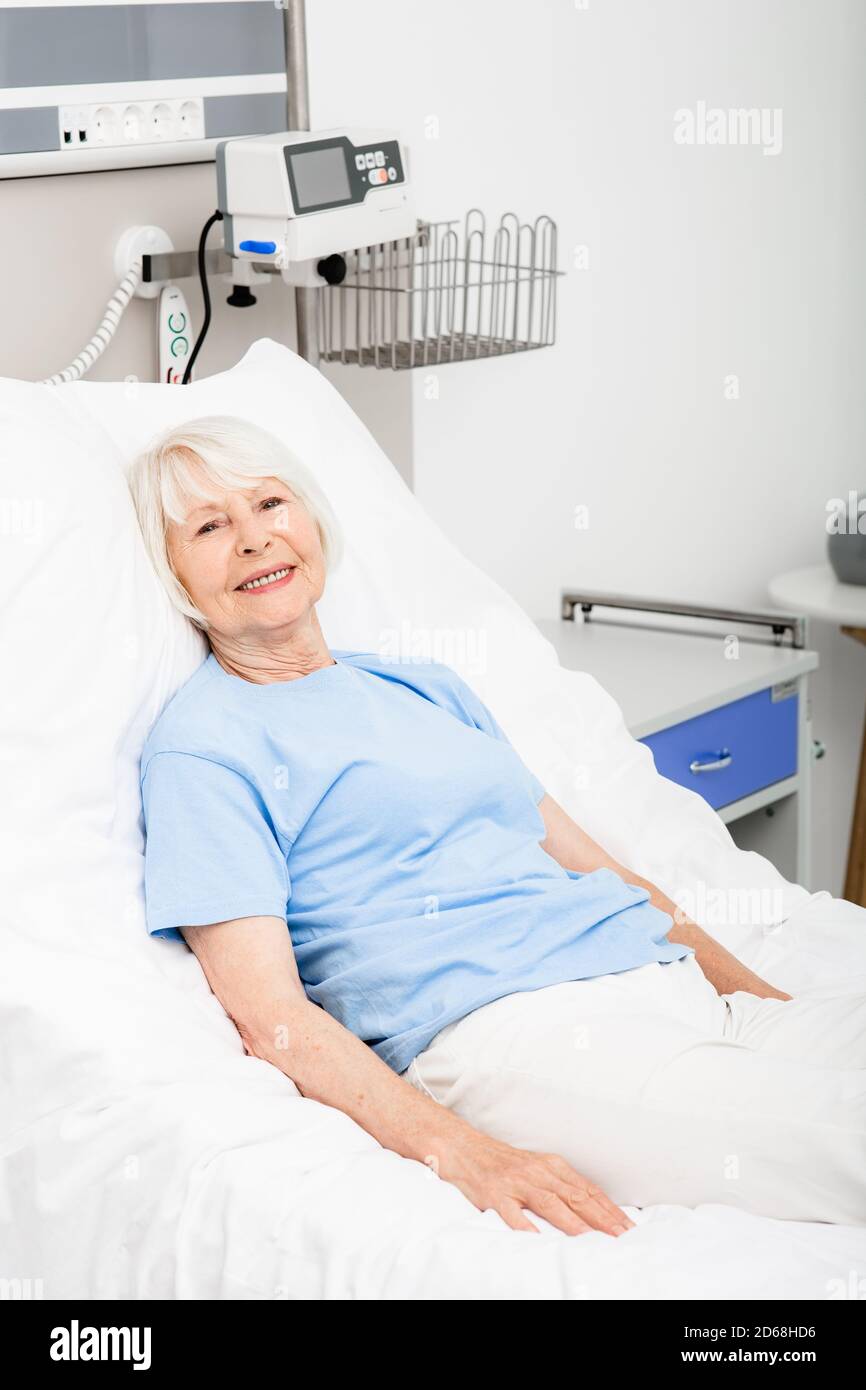 Ältere Frau liegt in einem Krankenhausbett in einer positiven Stimmung, weil sie sich von ihrer Krankheit erholt hat und völlig gesund ist. Erschwingliches modernes Medikament Stockfoto