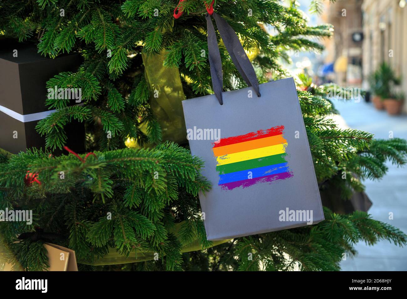 Regenbogen-LGBT-Flagge auf einer Weihnachts-Einkaufstasche als Dekoration auf einem Weihnachtsbaum auf einer Straße gedruckt. Stockfoto