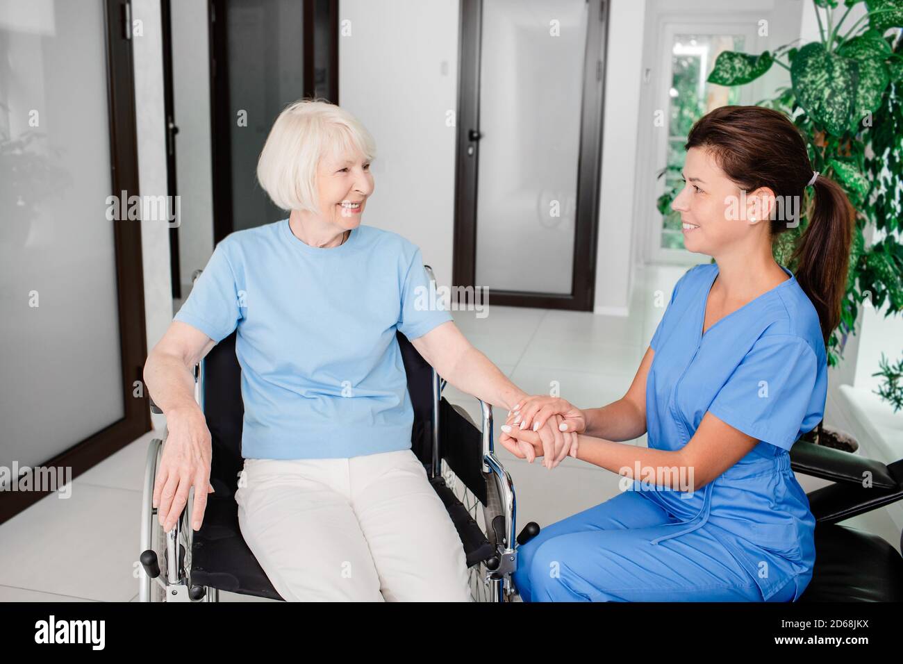 Lächelnde Krankenschwester und ältere Patientin im Rollstuhl. Medizinische Versorgung von Menschen mit Behinderungen Stockfoto