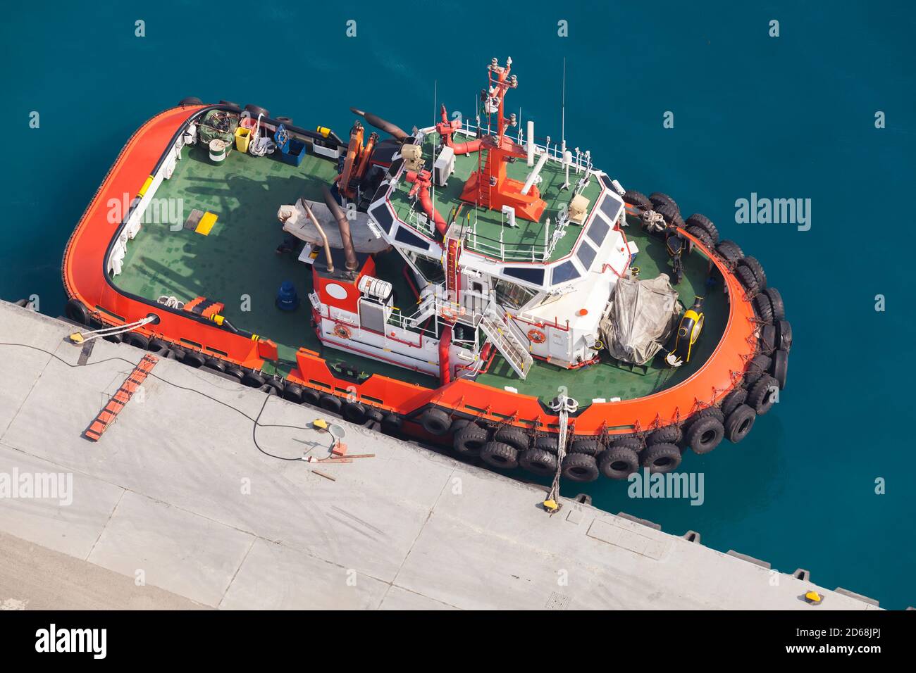 Schlepper mit leuchtend orangefarbenem Rumpf und grünem Deck ist in einem Hafen vertäut. Luftaufnahme Stockfoto