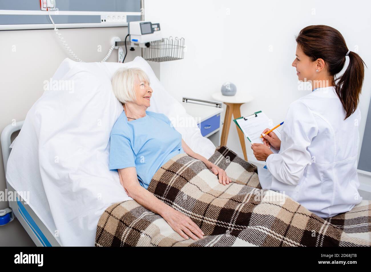 Der Arzt erklärt den Behandlungstermin, während er im Krankenhausbett eines älteren Patienten sitzt. Rehabilitation nach Herzinfarkt, Schlaganfall Stockfoto
