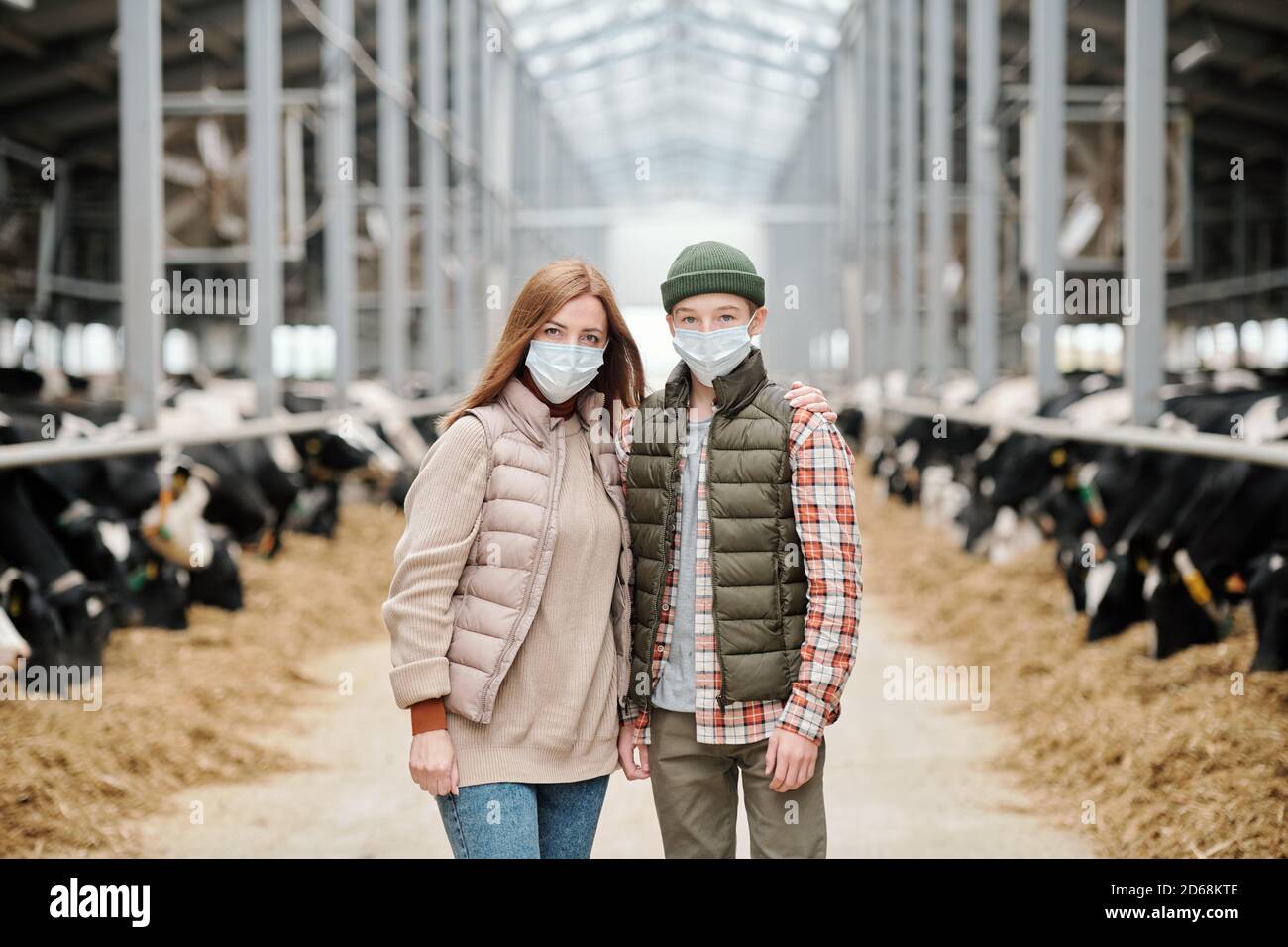 Portrait der Mutter umarmt Teenager-Sohn in Maske, während sie Stehen in großen Kuhstall Stockfoto