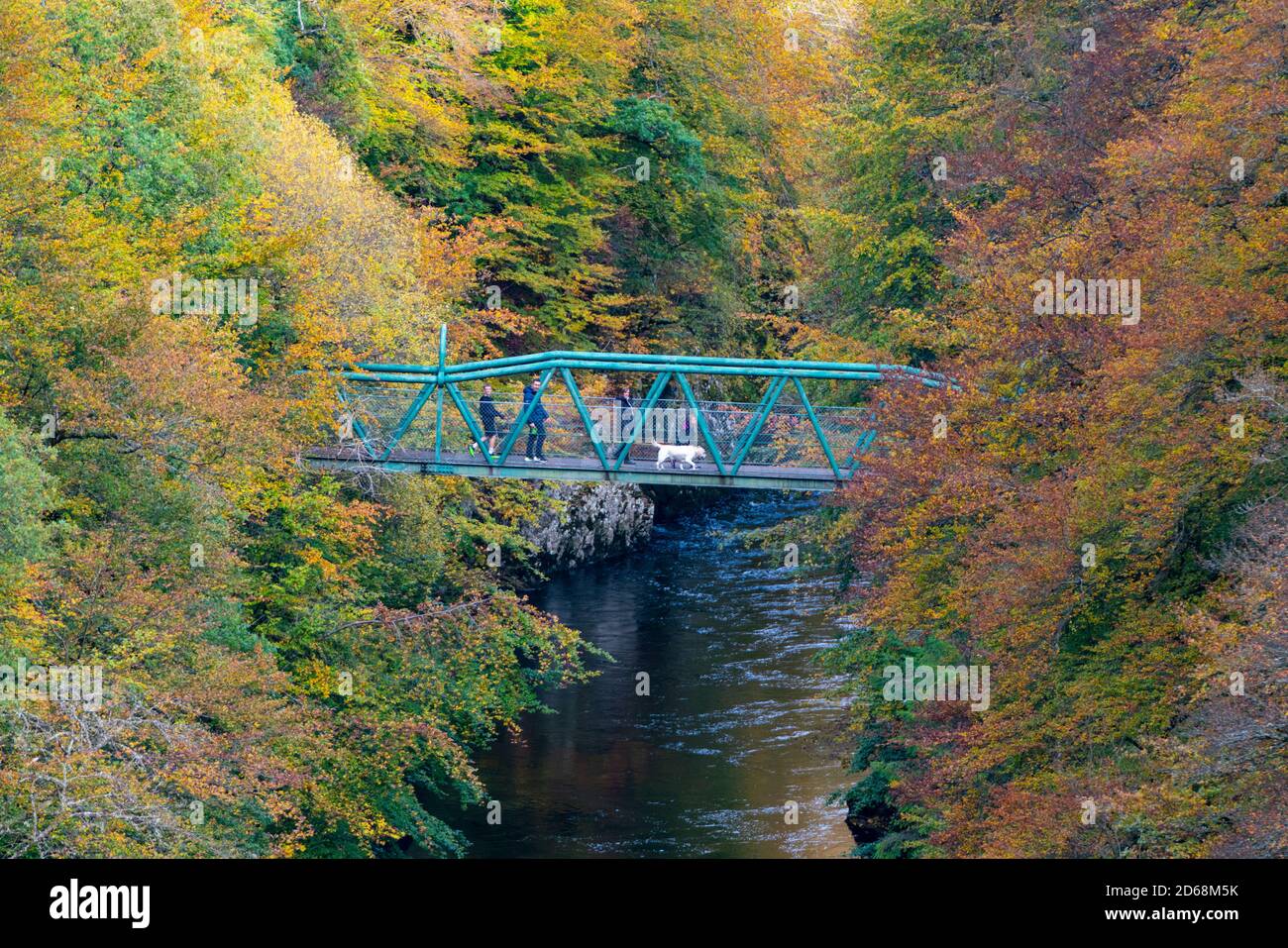 Besucher bewundern die Aussicht von der Fußgängerbrücke mit Herbstfarben auf Bäumen rund um den Fluss Garry an der Garry Bridge in der Nähe von Killiecrankie, Schottland, Großbritannien Stockfoto