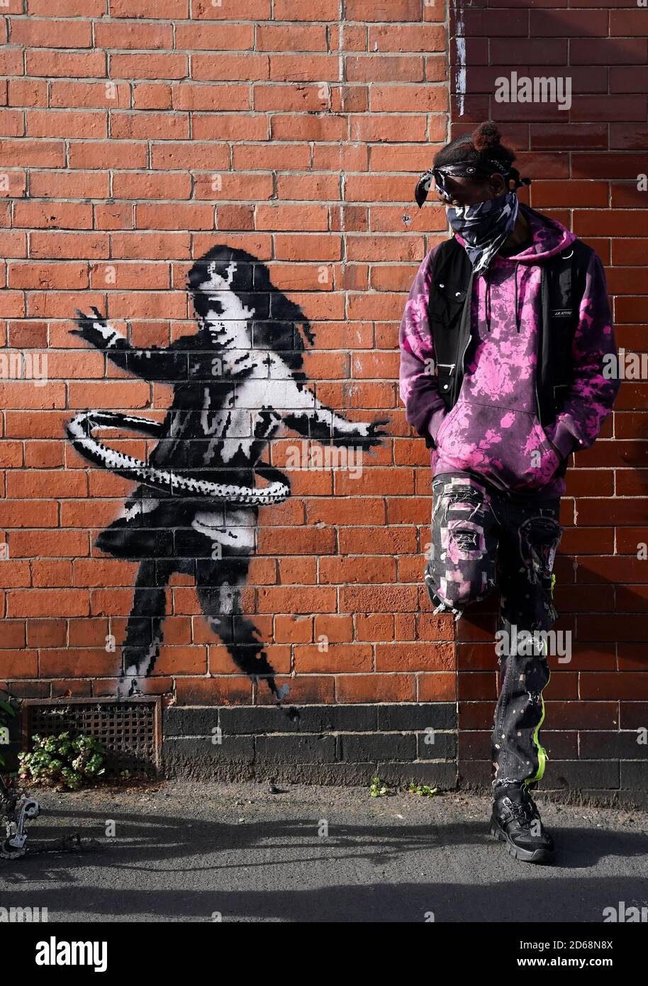 Der Nottingham-Bewohner Phidizz posiert für ein Foto neben Graffiti-Kunstwerken, die jetzt als das Werk des Straßenkünstlers Banksy bestätigt werden, auf einer Seite eines Grundstücks an der Rothesay Avenue und der Ilkeston Road, Nottingham. Das Kunstwerk zeigt ein junges Mädchen, das mit einem Reifen spielt, und ist auf einer Wand in der Nähe eines verlassenen Fahrrads gemalt, dem ein Rad fehlt. Stockfoto