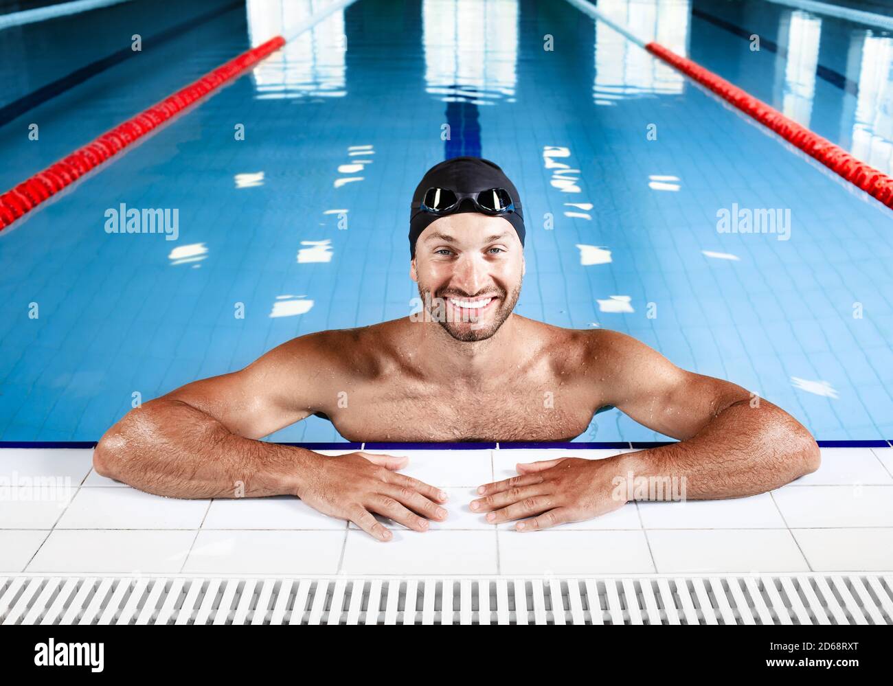 Positive Schwimmer, trägt Schwimmbrille und Badekappe, entspannen im Pool nach dem Training. Mann, der am Pool posiert Stockfoto